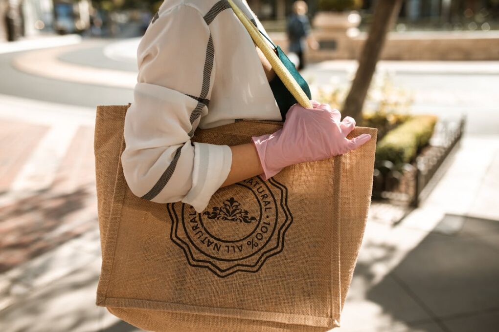 Free Close-up of a person with a brown tote bag and pink glove, outdoors on a sunny day